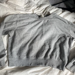 Grå sweatshirt från H&M i storlek M - En enkel och stilren grå sweatshirt från H&M i storlek M. Tröjan har rund hals, ribbade muddar vid ärmslut och nederkant samt långärmad passform. Perfekt för chill dagar och passar till allt. Mjuk insida och klassisk look. 