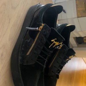 Giuseppe Zanotti - Snygga svarta sneakers från Giuseppe Zanotti med guldfärgade dragkedjor och signaturdetalj på plösen. Storlek 44 pris kan diskuteras