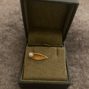 MariaNilsdotter örhänge⭐️ - 💖Unikt örhänge i guld med en elegant vinge och en vit pärla. Designen är stilren och detaljrik, perfekt för dig som vill ha något speciellt. Säljs i originalask.💖