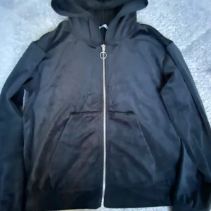 Svart hoodie med dragkedja från lager 157 - Svart hoodie från lager 157 med hel dragkedja och huva. Tröjan har två stora fickor framtill och är tillverkad i mjukt material som känns skönt mot huden. Perfekt för chill dagar eller när du vill ha en enkel och stilren look.