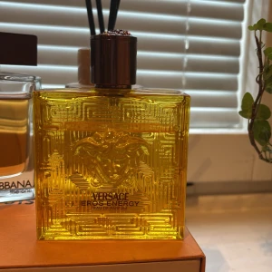 Versace Eros Energy Eau de Parfum - Versace Eros Energy Eau de Parfum i en fyrkantig, guldfärgad glasflaska med Medusa-huvudet ingraverat på framsidan. Flaskan har ett elegant mönster och en mörk kork som ger en lyxig känsla. Perfekt för dig som gillar exklusiva dofter.
