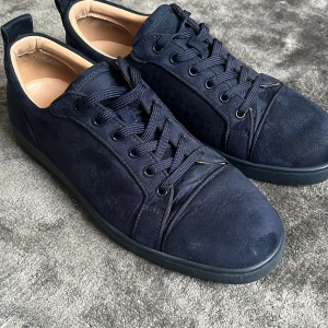Mörkblå loobs - Snygga mörkblå sneakers i mocka från Christian Louboutin med klassisk röd sula och svarta snören. Skorna har rund tå, platt sula och beige innersida. Perfekta för dig som vill sticka ut med en lyxig touch.