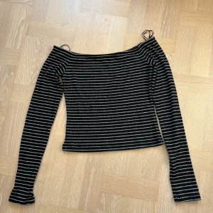 Randig offshoulder topp - Svart och vit randig offshoulder topp från Noisy May. Toppen har långa ärmar, smala axelband och är ribbad i materialet. Croppad passform som passar perfekt till jeans eller kjol.