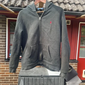 Svart hoodie från Polo Ralph Lauren - 🖤✨ Säljer en svart hoodie från Polo Ralph Lauren – klassisk och tidlös design. 🔥 Perfekt för dig som vill ha en bekväm & stilren vardagslook.  👕 Detaljer: Dragkedja framtill, huva & känguruficka. 🏷 Logga: Ikonisk liten röd broderad Polo-logga på bröstet.  📏 Storlek: Märkt 18–20 (motsvarar ungefär S).  ✅ En hoodie som kombinerar komfort, kvalitet & ikonisk stil – ett måste i garderoben!