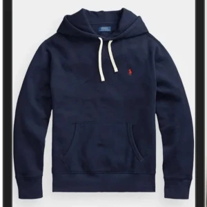 Marinblå hoodie från Polo Ralph Lauren - Snygg marinblå hoodie från Polo Ralph Lauren med vit snörning i huvan och klassisk röd logga på bröstet. Tröjan har känguruficka och ribbade muddar. Perfekt för en chill och stilren look.