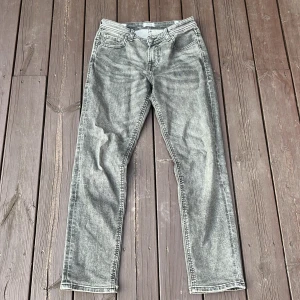 Grå jeans från Jack & Jones, stl 158 - Snygga grå jeans från Jack & Jones i storlek 158. Jeansen har en klassisk femficksmodell och raka ben. Färgen är tvättad grå med en cool, lite sliten look. Perfekta för dig som gillar en avslappnad och stilren vibe.