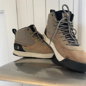 Beige boots från The North Face - Boots från The North Face i beige och svart med DryVent-teknologi. Ovandel i mocka och textil, svart tåparti och häl, samt vit sula. Skorna har snörning med svartvita skosnören och rund tå. Perfekta för dig som gillar outdoor och streetstyle. Ny pris 2000kr