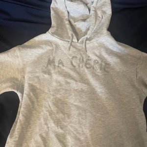 Grå hoodie med texten MA CHERIE - Grå Ma chérie hoodie från gina tricot. Använd fåtal ggr men i superbra skick!  Utan fläckar eller annat. Storlek 158/164 men passar mig som har s. Tvättar allt innan, skriv för mer bilder.💞 
