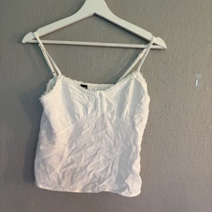 Vit linnetopp med spets från SHEIN - Söt vit linnetopp från SHEIN med tunna axelband och spetsdetaljer längs urringningen. Toppen har en liten knapp framtill och är i ett lätt material som passar perfekt till varma dagar. Enkel och stilren design som är lätt att matcha.