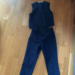 Mörkblå kostymväst och byxor - Snygg mörkblå kostymväst med matchande kostymbyxor. Västen har tre knappar framtill och två fickor, byxorna har klassisk passform med hällor för bälte. Perfekt för dig som vill ha en stilren och enkel look.