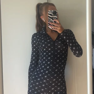Svart mönstrad långärmad set  - Säljer ett set med vitt grafiskt mönster och halv dragkedja framtill. Dressen  är tight och har en matchande jacka till. En sportig och trendig look. Perfekt för dig som gillar att sticka ut med stilrena detaljer. Både jackan och dressen är i storlek xs. Och säljs som ett set. 