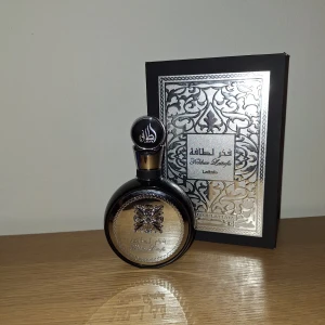 Lattafa Fakhar Lattafa Parfym - Exklusiv parfym från Lattafa, Fakhar Lattafa, i en rund svart flaska med silverdetaljer och orientaliskt mönster. Flaskan har en dekorativ silverplatta framtill och matchande svart-silver lock. Kommer i en snygg svart ask med silvermönster. Det fins cirka 70ml