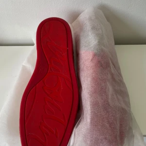Christian Louboutin sneakers  - Snygga röda sneakers från Christian Louboutin i mocka med ikoniska röda sulor och coola nitar framtill. Skorna har snörning och en clean, modern look som sticker ut. Perfekta för dig som vill ha något extra och vågar köra på färg.