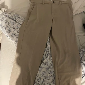 Beige kostymbyxor från Jack & Jones - Snygga beige kostymbyxor från Jack & Jones Pants Studio i relaxed fit. Byxorna har klassisk design med snedställda fickor fram och passpoalfickor bak. Perfekta för en clean och stilren look. Tillverkade i ett mjukt bomullsmaterial.