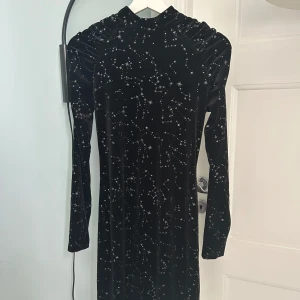 Svart sammetsklänning med silvrigt stjärnmönster - Supersnygg svart kort sammetsklänning från Lindex med långa ärmar och  stjärnmönster över hela klänningen. Axelpartiet har rynkade detaljer. Använd fåtal ggr