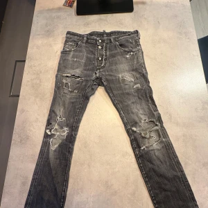 Grå slitna jeans från Dsquared2 - Riktigt snygga grå jeans från Dsquared2 med slitningar och trasiga detaljer på benen. Jeansen har knäppning med tre knappar framtill, klassisk femficksmodell och coolt tvättad look. Perfekta för dig som gillar streetstyle och vill sticka ut.