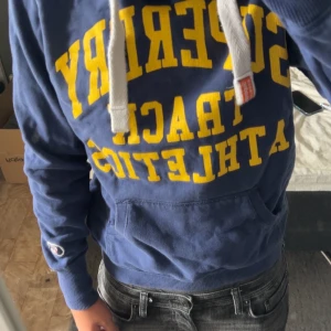 Blå Superdry hoodie med gula tryck - Superdry | Strl:M | Bra skick | Nypris: 699kr | Mitt pris: 399kr | Hör av dig vid funderingar🍀| OBS! texten har sprickor |