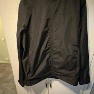 Svart vindjacka från Everest, M - Svart vindjacka från Everest med huva och dragkedja framtill. Jackan har en clean look, meshfoder på insidan och justerbar nederkant med snörning. Perfekt för blåsiga dagar och enkel att matcha med allt. Snygg och funktionell för dig som gillar stilren outdoor. Pris är inte fast skicka iväg ett meddelande vid frågor. My pris är ca 700. Jackan är i ett suveränt skick. Fler och bättre bilder går självklart att få. 