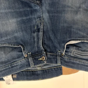 Blå jeans från Don dup george - Snygga blå jeans från Domdup George modellen  med klassisk femficksdesign och diskret logga bak. Jeansen har en rak passform och är tillverkade i slitstarkt denim med lätt tvättad look och kontrastsömmar. Perfekta för dig som gillar en stilren och avslappnad vibe.