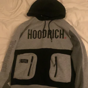 Grå och svart hoodie från Hoodrich XS - Säljer en grå och svart hoodie från Hoodrich i storlek XS. Tröjan har stor logga framtill, två fickor med dragkedja och snörning i huvan. Hoodien har lång ärm och coola tryck på både ärm och rygg. Perfekt för dig som gillar streetwear och vill sticka ut. Storlek XS men passar S, om du är storlek M så är den lite för liten men funkar