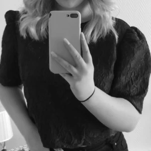 Svart blommig blus från Lindex - Supersnygg svart blus från Lindex med puffiga ärmar och blommigt strukturmönster i tyget. Croppad modell med rund halsringning och korta ärmar. Perfekt för dig som vill ha en trendig och stilren look.