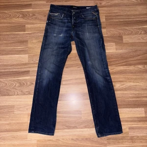 Replay Waitom blå jeans straight fit - Snygga Replay Waitom jeans i klassisk blå tvätt med slitningar och raka ben. Jeansen har fem fickor, tydliga kontrastsömmar och Replay-logga på fickan. Tillverkade i slitstarkt bomullsjeansmaterial och passar perfekt till en avslappnad streetstil.
