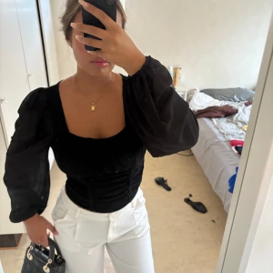 Svart blus med puffärmar - Säljer en svart blus med fyrkantig ringning och långa puffärmar. Toppen har figurnära passform över bålen och är sydd i ett lätt, tunt material som ger en snygg siluett. Perfekt att styla med både jeans och kjol för en trendig look.