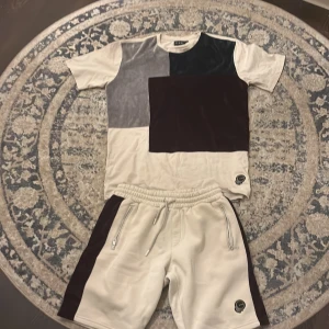 La vichy set - Snygga beige shorts och t shirt från LAvichy med breda vinröda sammetspaneler längs sidorna på shortsen, och i mitten på t shirten. De har elastisk midja med snörning och två dragkedjeförsedda fickor. Materialet är mjukt och har en lyxig känsla, perfekt för chill dagar. Patch med logga på benet.