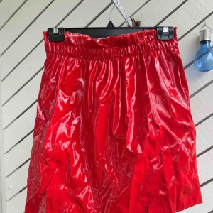  - En skinnkjol i röd lack färg. Strl:M  Resår i midjan, elastisk , väldigt bekväm att ha på! Helt ny med etikett på!  Köparen står för frakten! 