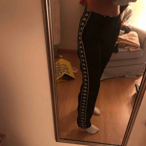  - Svarta kappa byxor där de är ett kappa märke på ena sidan och på andra sidan står de kappa längst benet. 