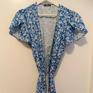 Blommig, oanvänd klänning - Oanvänd klänning med omlottknyt. 