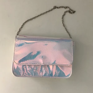 Väska kort band - En gullig liten väska i holographic-färg. Bandet är egentligen långt (axelrämsväska) men jag har knutit det kort (går att knyta upp). Frakt tillkommer 🥰