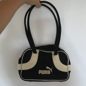 Puma handväska - Snygg, 90’s handväska från Puma! ”Läder”-delarna har några skavanker, se bilder. Ca 20x15 cm, svartvit. ”REA” på alla annonser! 2 varor 10%, 3 varor 15%, 4 eller fler varor 20%!  45kr frakt oavsett antal varor, om varan är lätt sänks frakten. Jag ansvarar inte för postens slarv.