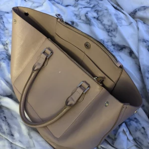 Väska - Säljer denna ljusrosa / beiga väska vet inte riktigt vart den är ifrån men jätte fin och stort utrymme. Har en liten spegel som en liten detalj som hänger ut på ena sidan! 