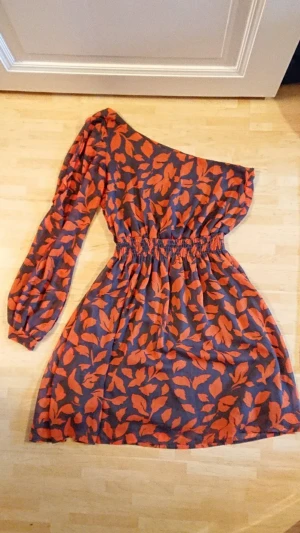 Off the shoulder-klänning - Orange och grå blommig klänning i polyester. Över knäna. Skriv gärna till mig om du önskar fler foton! Betalning via swish. Köparen står för frakt om vi inte kan mötas upp i Stockholm.