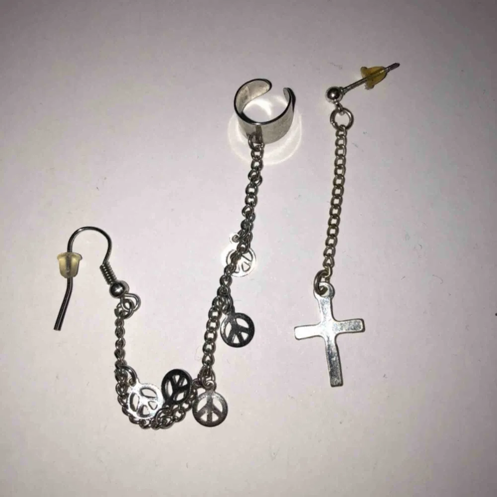 Ett speciellt par örhängen. Den ena delen är ett kors och den andra är ett hänge med peacemärken som man sätter i örsnibben och även högre upp på örat som en helix. Köparen betalar frakten. Accessoarer.