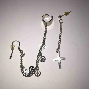  - Ett speciellt par örhängen. Den ena delen är ett kors och den andra är ett hänge med peacemärken som man sätter i örsnibben och även högre upp på örat som en helix. Köparen betalar frakten