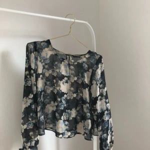  - Knapp på ena armen har lossnat. Blommigt mönster. Blus