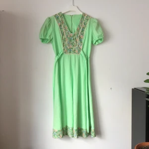  - Mintgrön vintageklänning med blommiga bårder. Blixtlås  i metall, så bör vara 60-tal, -68? Hemsydd, troligen efter mönster i nån tidning. Har släppt pyttelite i sömmen runt midjan, (se bild). 