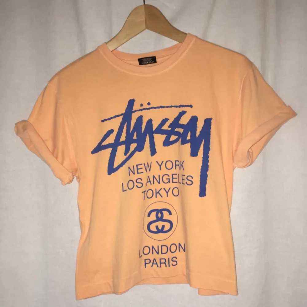 Snygg  persikofärgad Stüssy tröja med blå text + logga. Tröjan är uppsydd. . T-shirts.