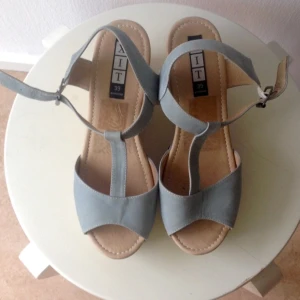  - Nästan helt nya sandaler med kilklack i trä och remmar i ljus grå/grönt. Äkta läder. Från XIT.