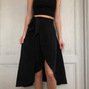 Midi-kjol - Svart omlott-kjol från Monki i strl 32. Jag skulle säga att den passar 34 oxå. Banden på ena sidan hjälper till att dra åt om man vill att den ska sitta tajt i midjan. Betalningen sker via swish🖤 (frakt 44kr)