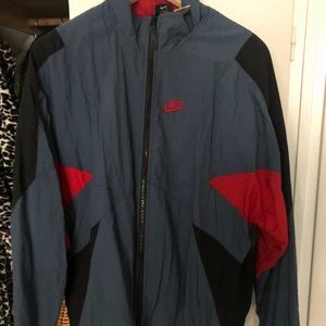 Vindjacka Nike - En blå/svart/röd tunn jacka från Nike! Köpte den här på plick men den har inte kommit till användning så säljer dräför vidare den. Den är ganska oversized på mig som har strl M i vanliga fall. Frakt och mötas i Malmö/Lund går bra (köpare står för frakt).