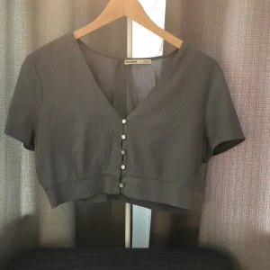 Topp med öppen rygg - Superfin cropped blus med knäppning där fram. Pärlemorskimrande knappar. Den har en nyckelhålsöppning på ryggen och är mellangrått tyg. Knappt använd så jag insåg att det var fel storlek för mig. (För tajt över bröstet). 