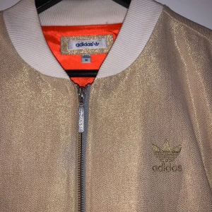 Adidasjacka - Unik och supersnygg adidasjacka i guld/persika-ish och vit/silver. Drömmig vårjacka. Säg till för fler bilder.