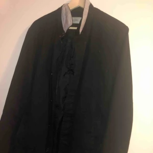  - Trenchcoat i svart färg. 