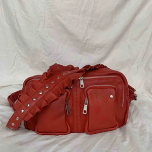  - Röd väska från Nùnoo i modellen Alimakka. Det är en limited edition väska med ett avtagbart band med volang. Det andra bandet är justerbart. Äkta kalvskinn. Väskan är i nyskick, använd mycket sparsamt. Nypris: ca 1600kr. 