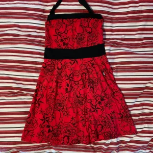 Rockabilly klänning - Rockabilly klänning, röd med dödskallar och rosor. Man knyter runt halsen. Aldrig använd, bara hänt i garderoben. Strl M/L. Tyget är töjbar och ”luftig”. Frakt tillkommer! 