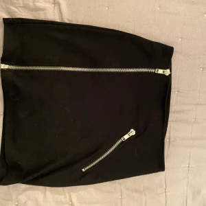 Kort svart kjol - Säljer den här korta svarta kjolen med små dragkedjor som detaljer. Den lilla på snedden går inte att öppna, men den stora långa går att öppna, använd några få gånger, liiiite nopprig. Pris går att diskutera 💓