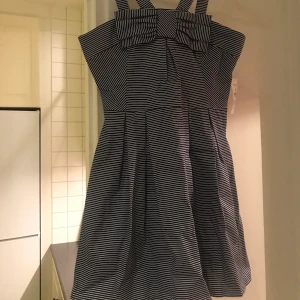 Klänning - Jättesöt klänning med rosett fram. Smalrandig i vitt och mörkblått. Oanvänd, lappen sitter kvar. Längd exkl axelband ca 62 cm. Ev lite liten i storleken. Köparen betalar frakt. Skriv om du har frågor 💙